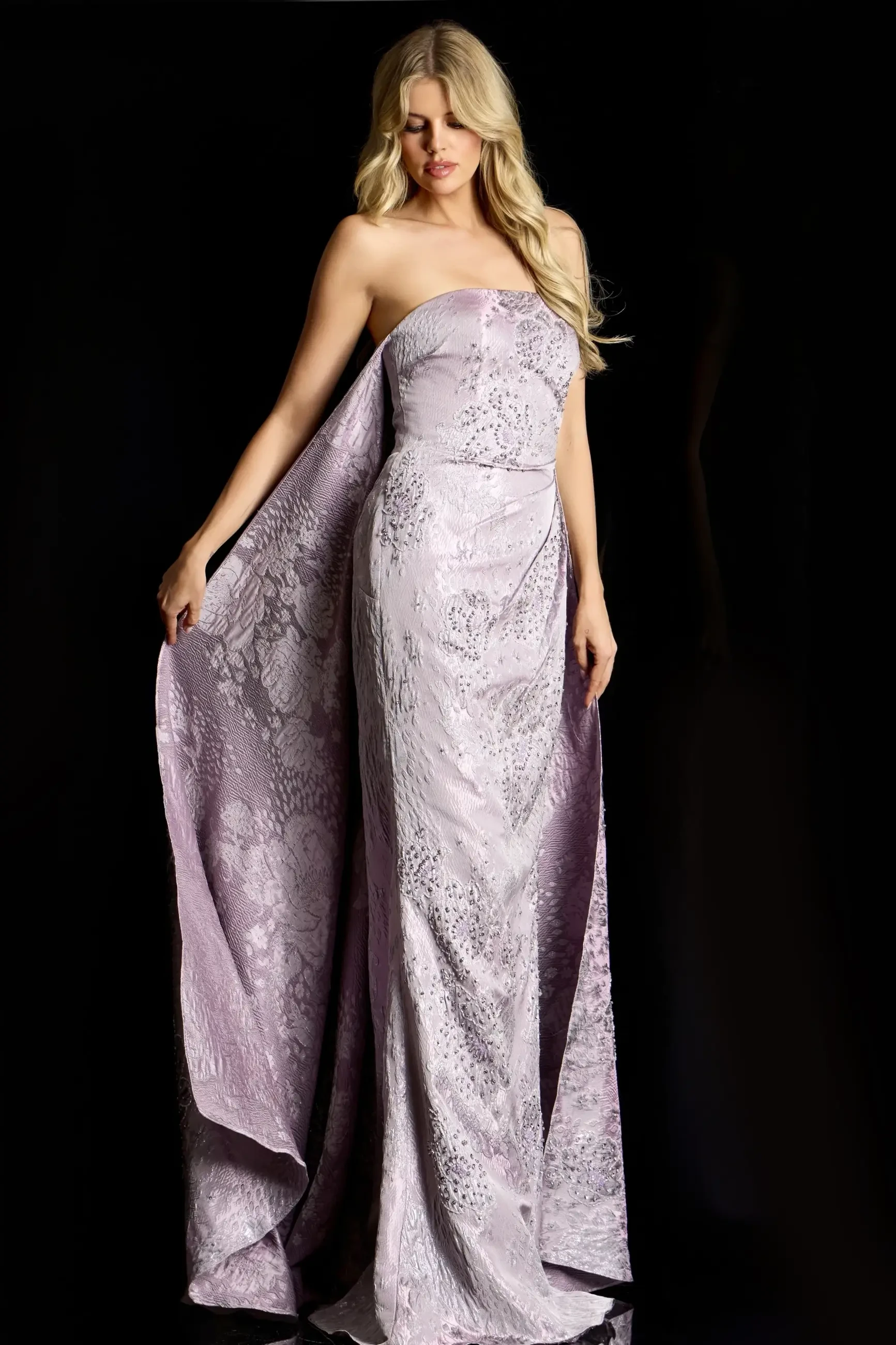 A woman wearing a strapless lavender gown with intricate patterns, standing against a black background.