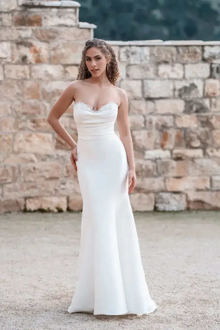 A woman wearing a strapless white dress standing in front of a stone wall.