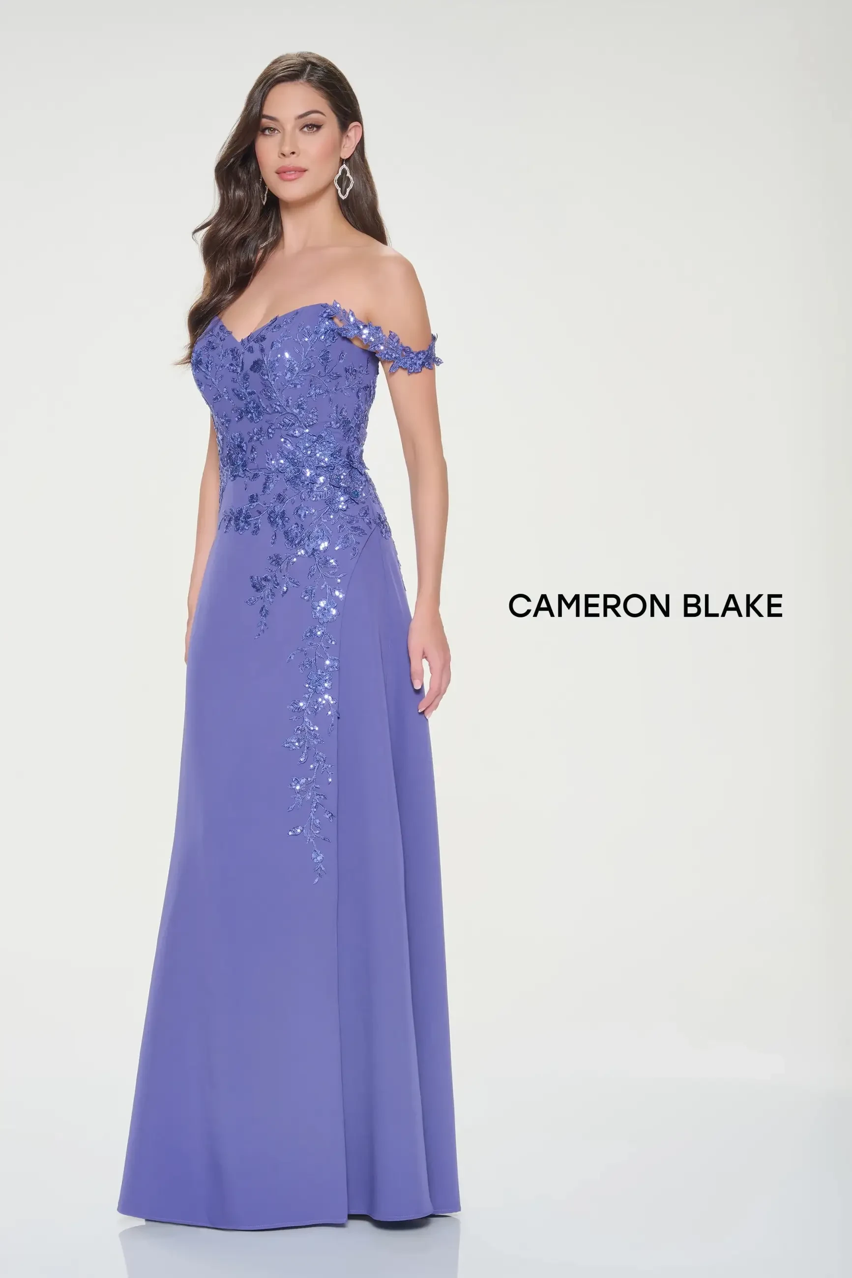 A woman wearing a purple off-the-shoulder gown with embellishments, posing elegantly.